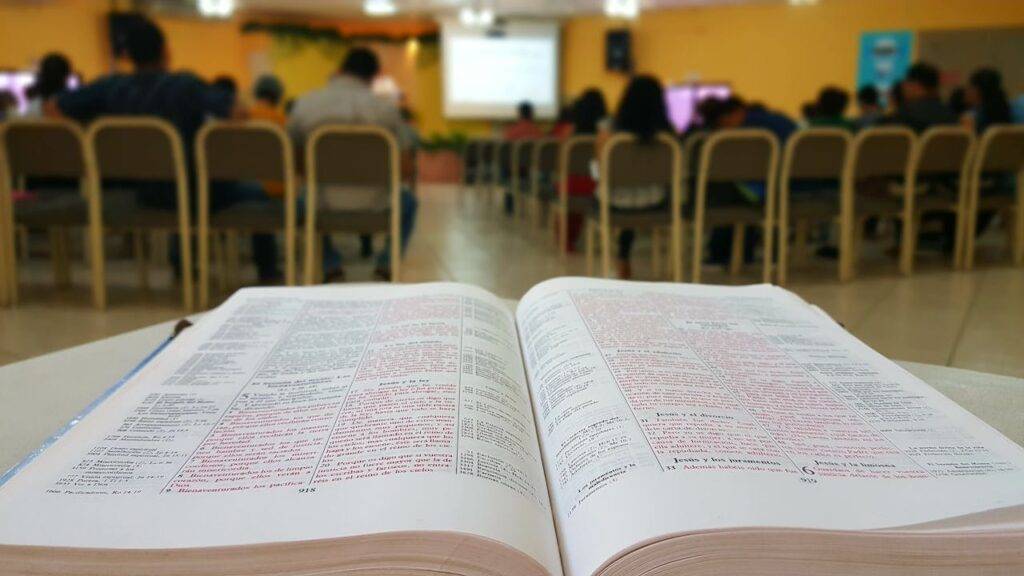 Open book in focus with a blurred group study session in the background.